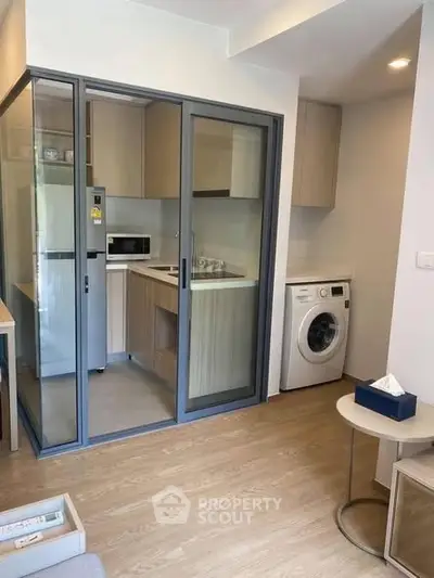 Modern compact kitchen with sliding glass doors and in-unit washing machine in cozy apartment.