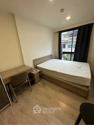 Cozy bedroom with wooden flooring, large window, and modern furniture in a stylish apartment.