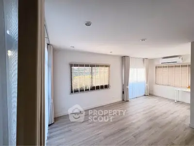 Spacious modern living room with large windows and wooden flooring, perfect for natural light and comfort.