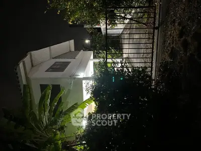 Charming two-story house with lush garden and night lighting, perfect for serene living.