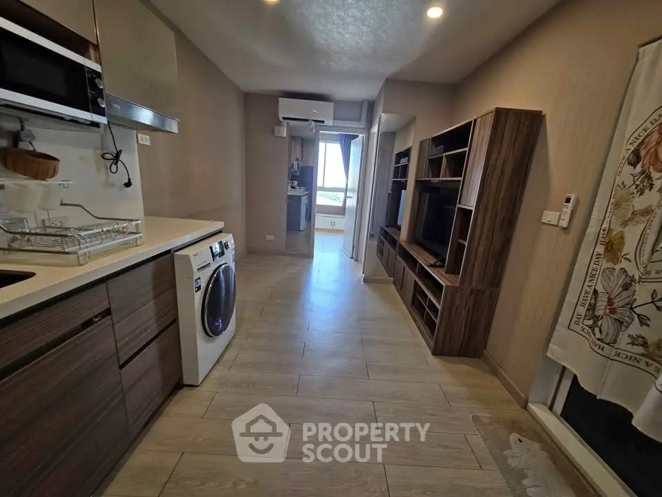 Modern kitchen with sleek cabinetry and in-unit washing machine, leading to a bright living area.
