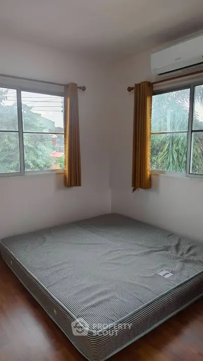 Cozy bedroom with large windows and air conditioning, featuring a comfortable mattress and wooden flooring.