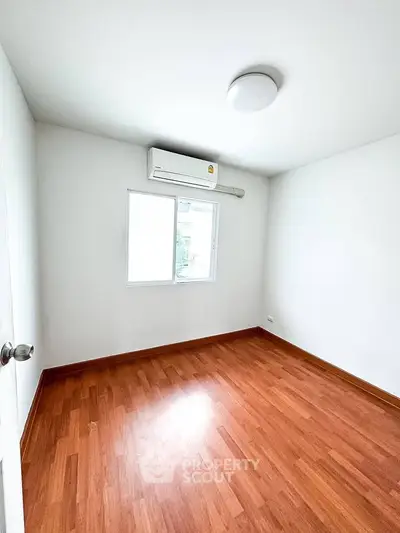 Spacious empty bedroom with wooden flooring and air conditioning.