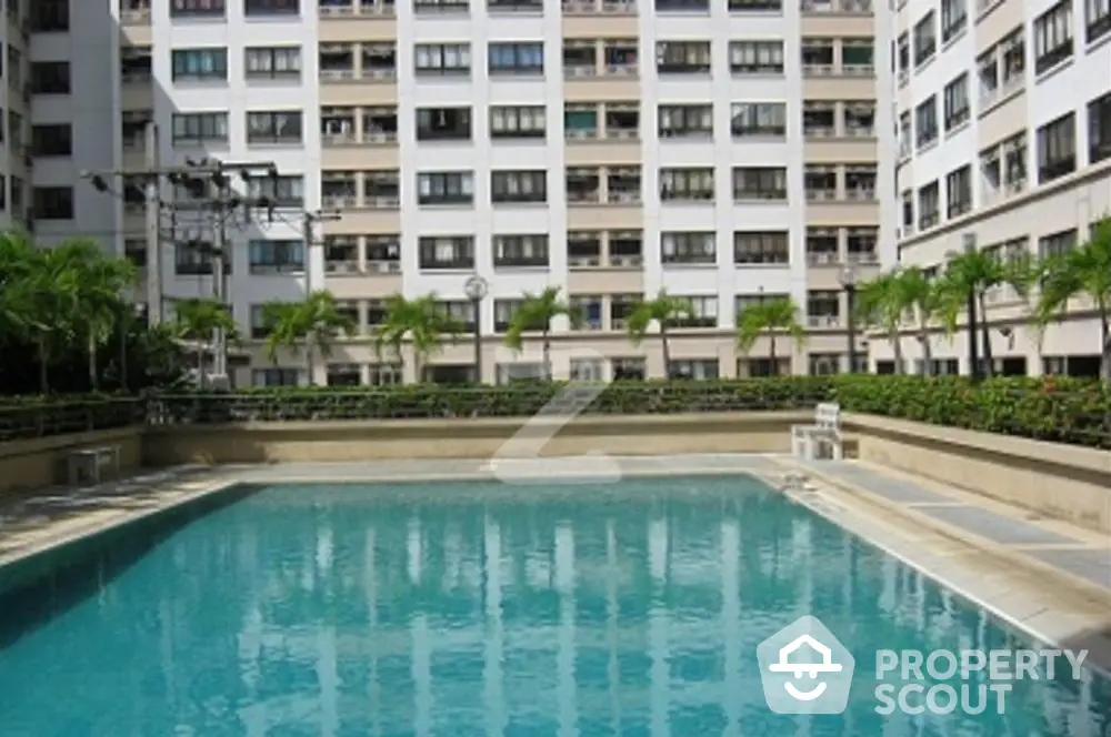 Inviting residential complex pool surrounded by lush greenery and a modern high-rise building, offering a tranquil urban oasis for relaxation and leisure.