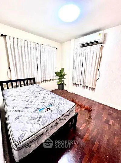 Spacious bedroom with hardwood floors and natural light, featuring air conditioning and modern decor.