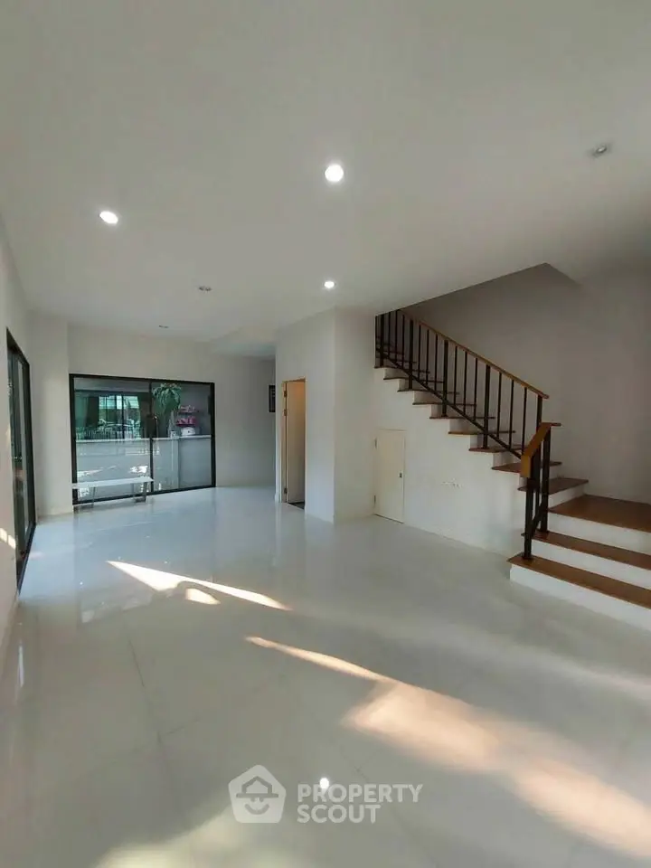 Spacious modern living room with large windows and staircase, perfect for family gatherings.