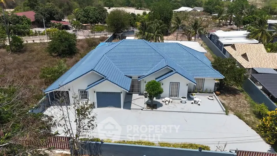 Stunning aerial view of a modern blue-roofed house with spacious driveway and lush surroundings.