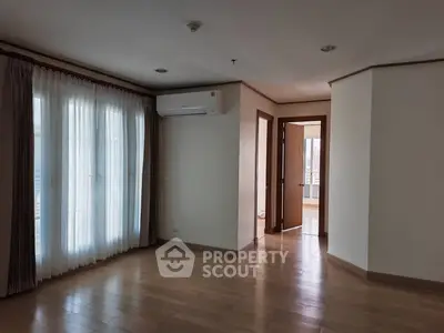 Spacious empty room with wooden flooring and large windows in modern apartment.