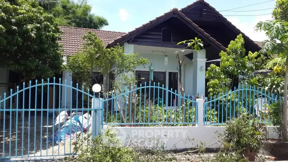 Charming single-story house with lush garden and blue fence, perfect for family living.