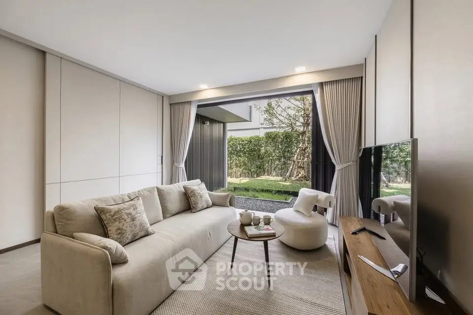 Modern living room with large sofa, flat-screen TV, and garden view through sliding glass doors.