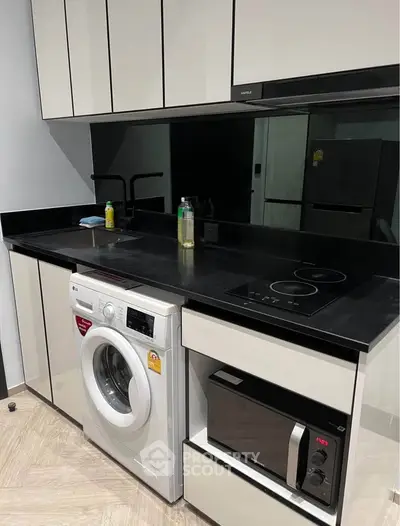 Modern kitchen with sleek black countertops, built-in appliances, and washing machine.