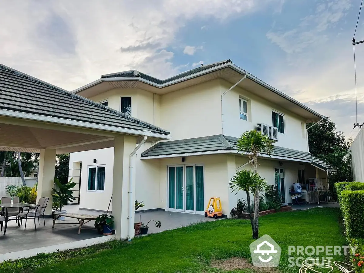 Spacious two-story family home with large windows and a lush green lawn, featuring a covered carport and a cozy outdoor seating area.