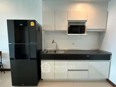 Modern kitchen with sleek black fridge and built-in microwave in stylish apartment.