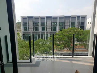 Modern apartment balcony with glass railing offering a scenic view of contemporary buildings and lush greenery.