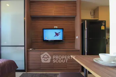 Modern living room with sleek wooden cabinetry and mounted TV, adjacent to a compact kitchen area.