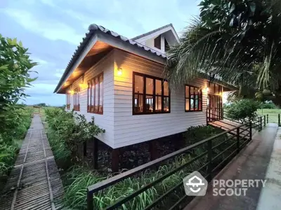 Charming tropical bungalow with warm lighting, surrounded by lush greenery and accessible via a quaint wooden walkway, offering a serene escape.