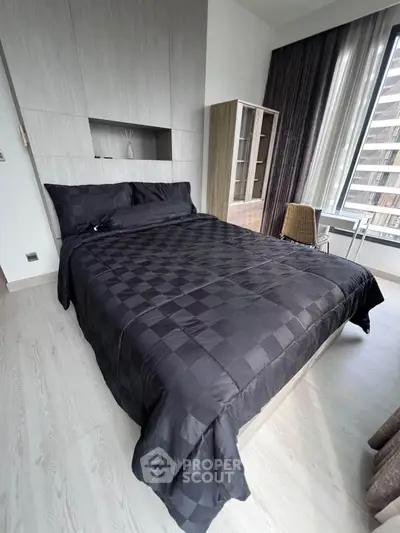 Modern bedroom with sleek black bedding and large window offering natural light.