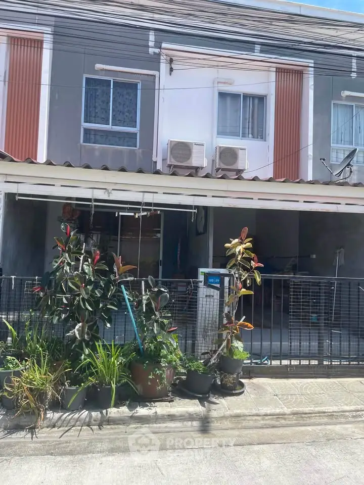 Charming townhouse exterior with lush garden and covered parking area.