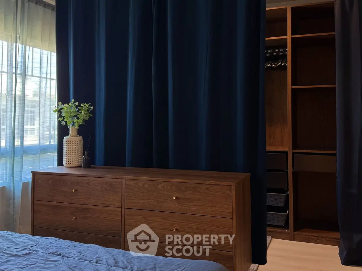 Elegant bedroom with wooden dresser and open walk-in closet, featuring dark curtains and natural light.