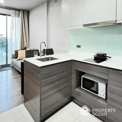 Modern kitchen with sleek cabinetry and built-in appliances opens to a cozy living area with ample natural light and balcony access, perfect for urban living.