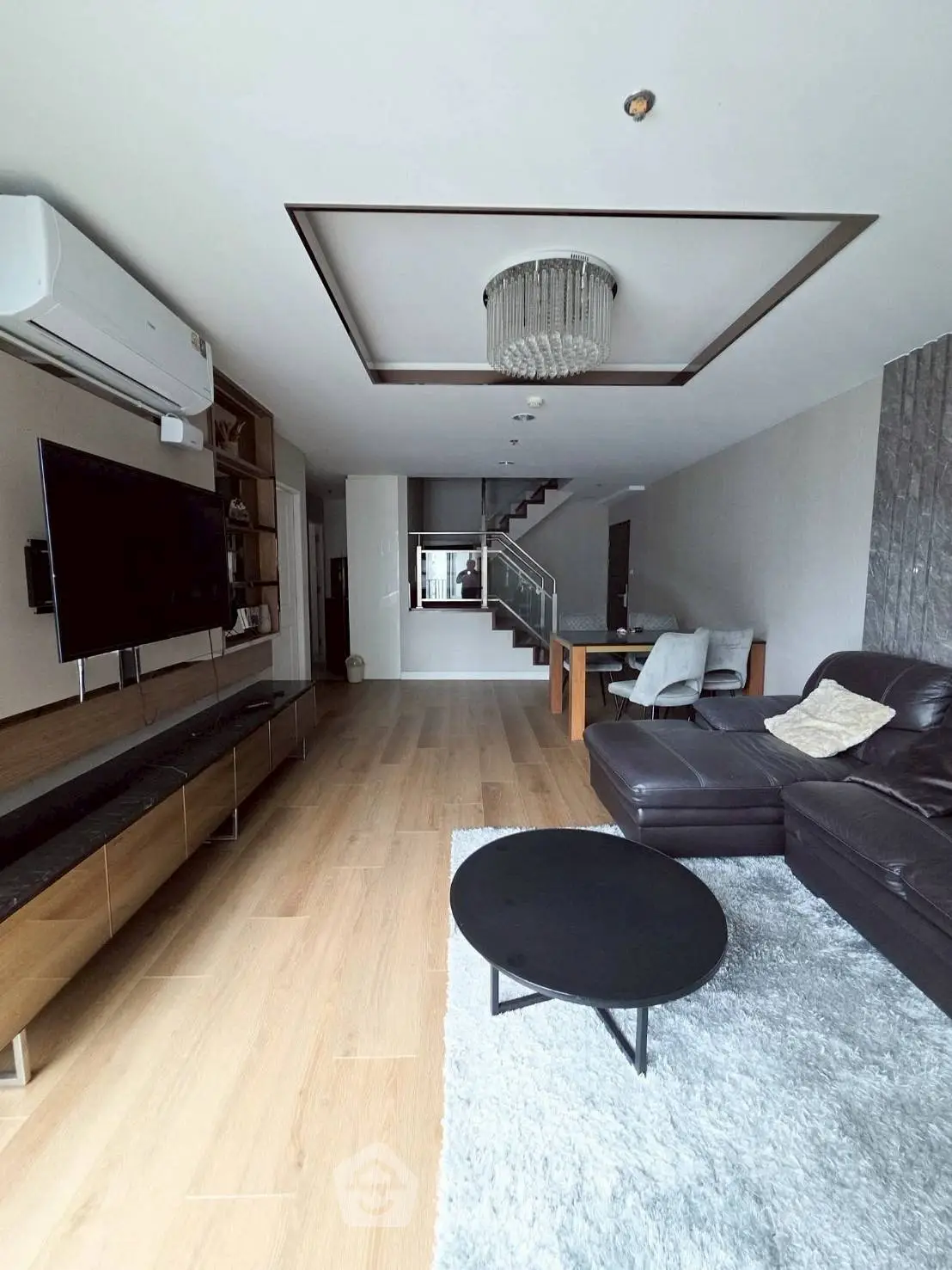 Spacious modern living room with leather sofa, flat-screen TV, and elegant chandelier in a stylish apartment.