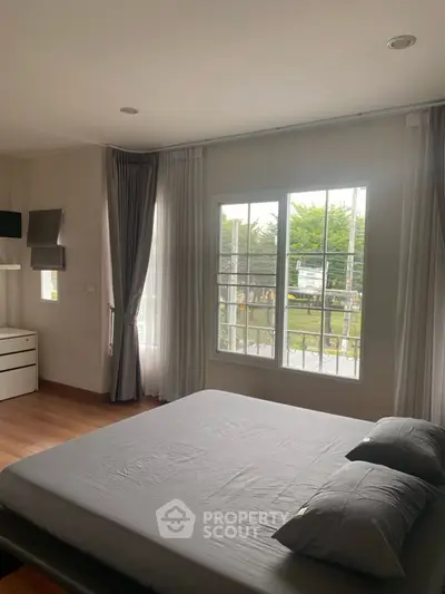 Spacious bedroom with large window and modern furnishings, offering a serene garden view.