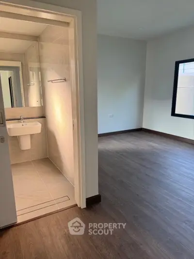 Modern apartment interior with bathroom and spacious room, featuring sleek flooring and large window.