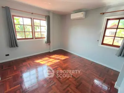 Spacious empty room with polished wooden floors and large windows in a bright home.