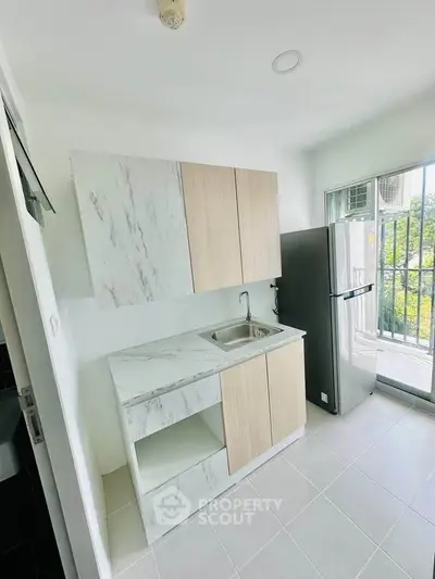 Modern kitchen with sleek cabinetry and balcony view, featuring a stainless steel fridge and marble countertops.