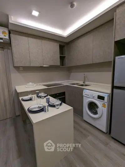 Modern kitchen with sleek cabinetry, washing machine, and dining setup in a compact space.