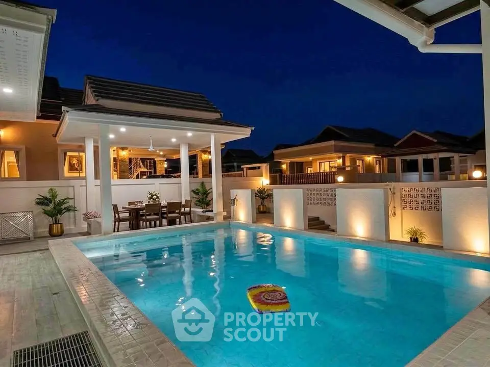 Luxurious villa with illuminated pool and elegant outdoor dining area at night.