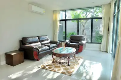 Bright and spacious living room with modern leather sofas and large windows overlooking greenery.
