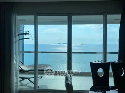 Stunning ocean view from modern apartment balcony with lounge chair and dining area.