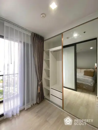 Modern bedroom with mirrored wardrobe and large window offering natural light.