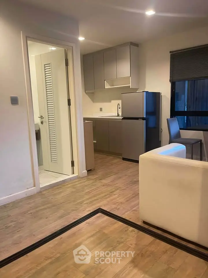 Modern apartment interior with compact kitchen and cozy living area, featuring sleek cabinetry and wood flooring.