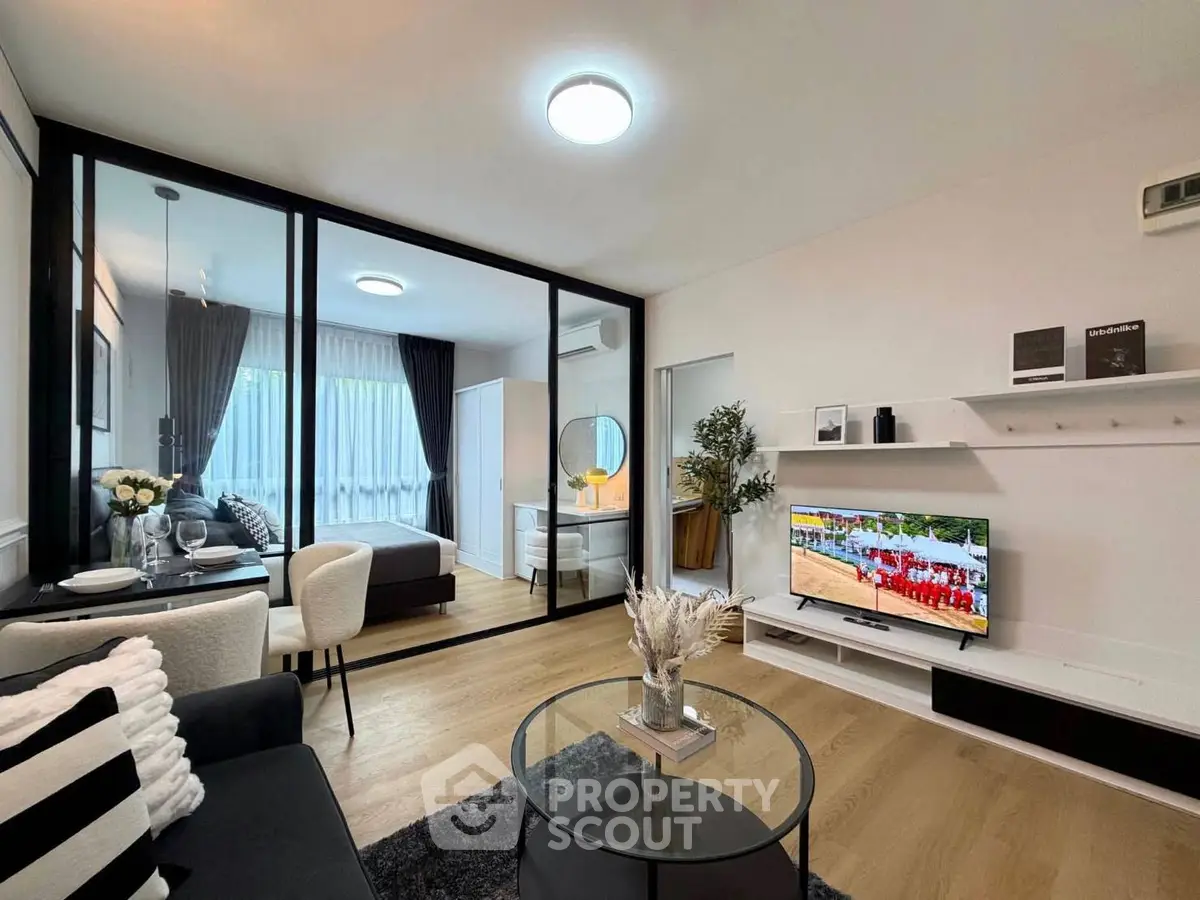 Modern living room with glass partition to bedroom, stylish decor, and flat-screen TV.