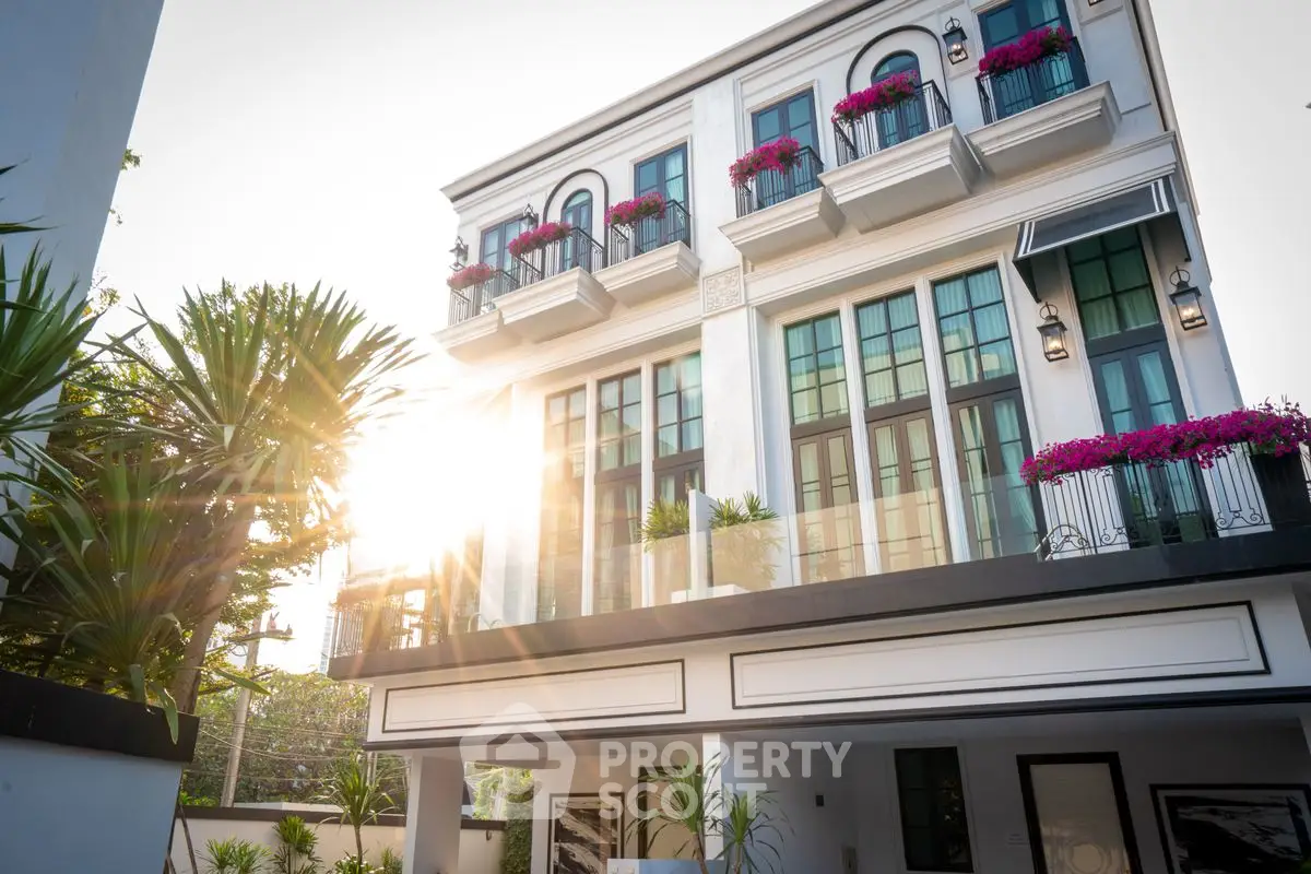 Elegant modern building with lush greenery and sunlit facade, featuring stylish balconies and large windows.