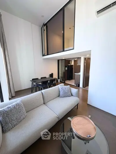 Modern living room with high ceiling and mezzanine, featuring stylish furniture and open layout.