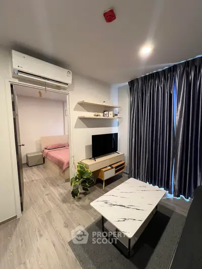 Modern living room with stylish furniture and natural light, featuring a view into a cozy bedroom.