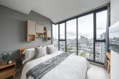 Modern bedroom with stunning city view through large windows, featuring stylish decor and cozy bedding.