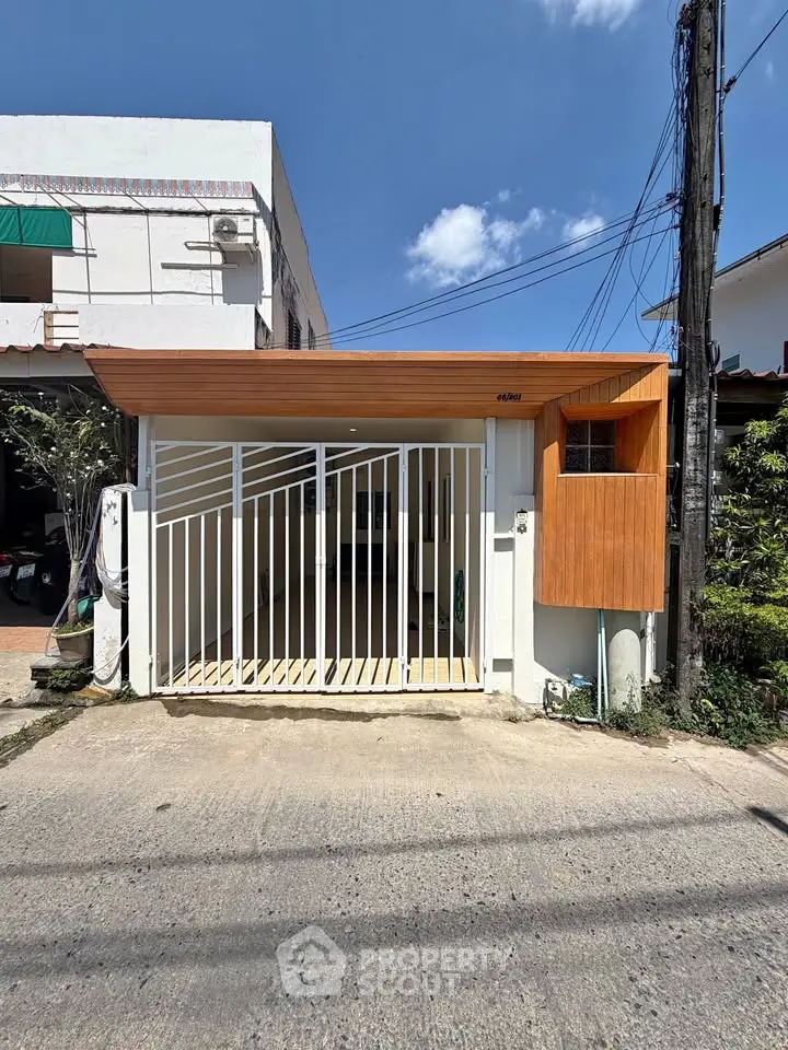 Modern minimalist house exterior with wooden accents and gated entrance under clear blue sky.
