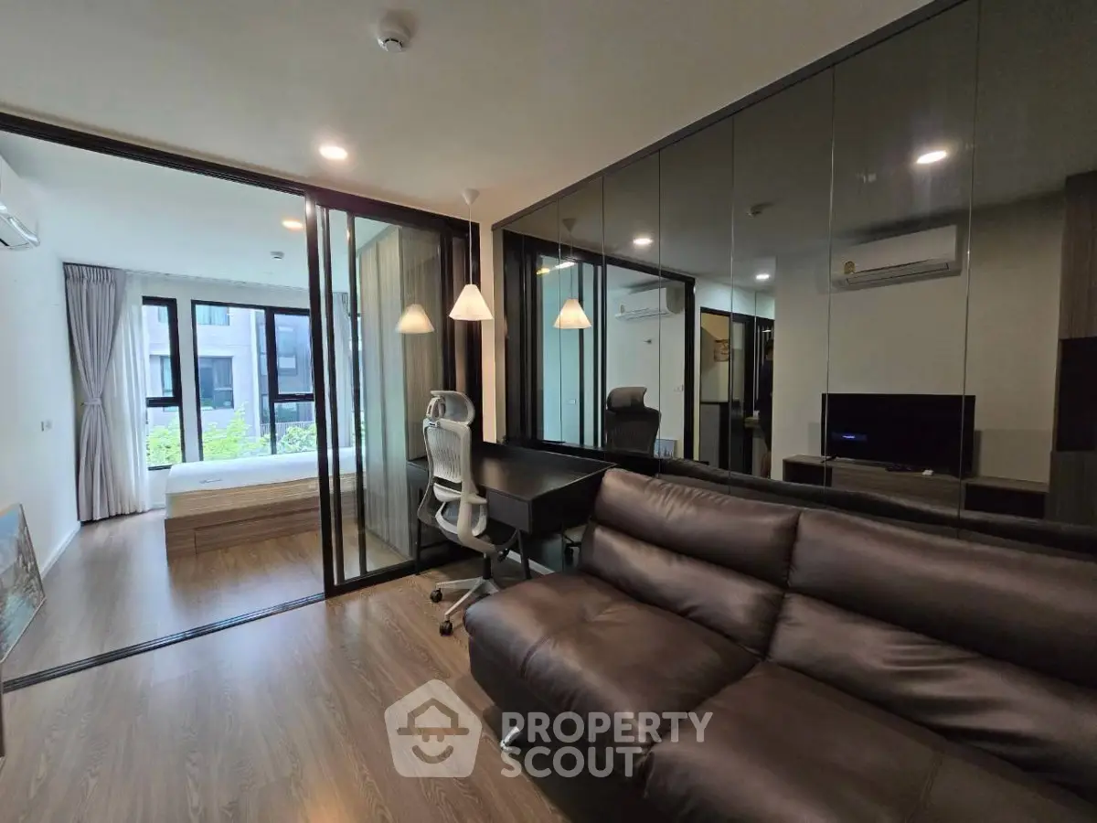 Modern living room with sleek design and glass partitions, featuring a comfortable sofa and work desk.
