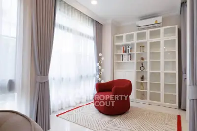 Elegant living room with modern red chair, stylish bookshelf, and large windows with sheer curtains.