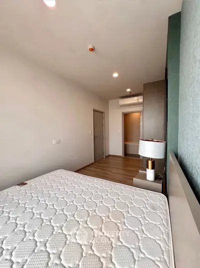 Spacious bedroom with modern decor and natural light, featuring a comfortable mattress and stylish lamp.