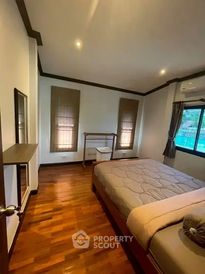 Spacious bedroom with wooden flooring and large windows in a modern home.