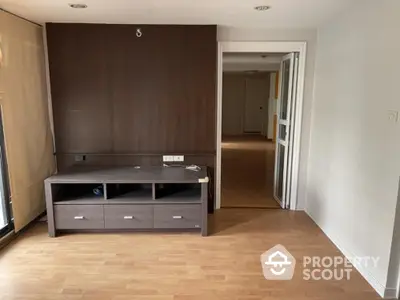 Spacious living room with elegant wooden flooring and a modern entertainment unit, leading to a well-lit corridor.