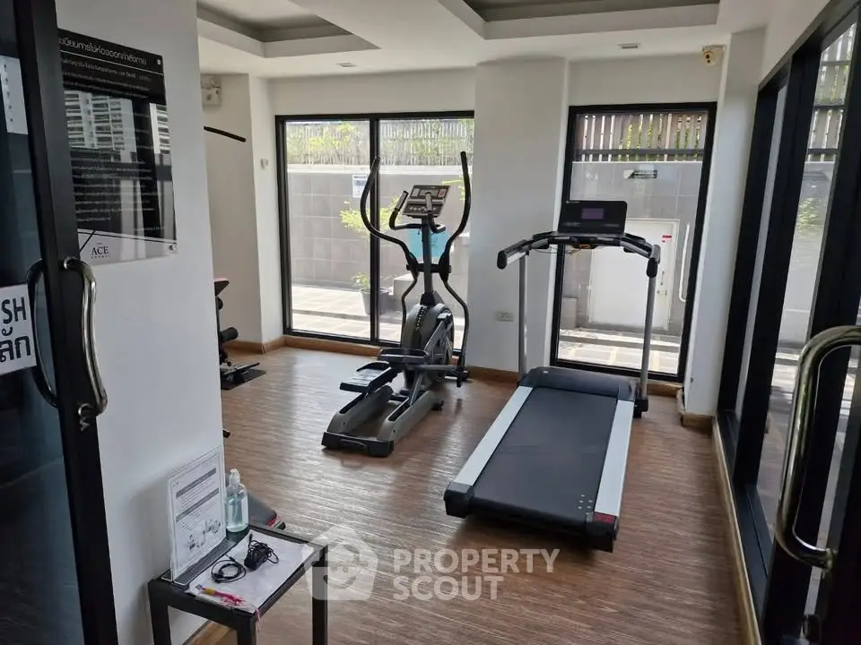 Modern gym with treadmill and elliptical in a bright, glass-walled room.