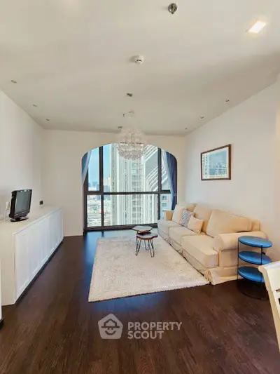 Spacious living room with hardwood floors, large windows offering city views, and elegant chandelier lighting.