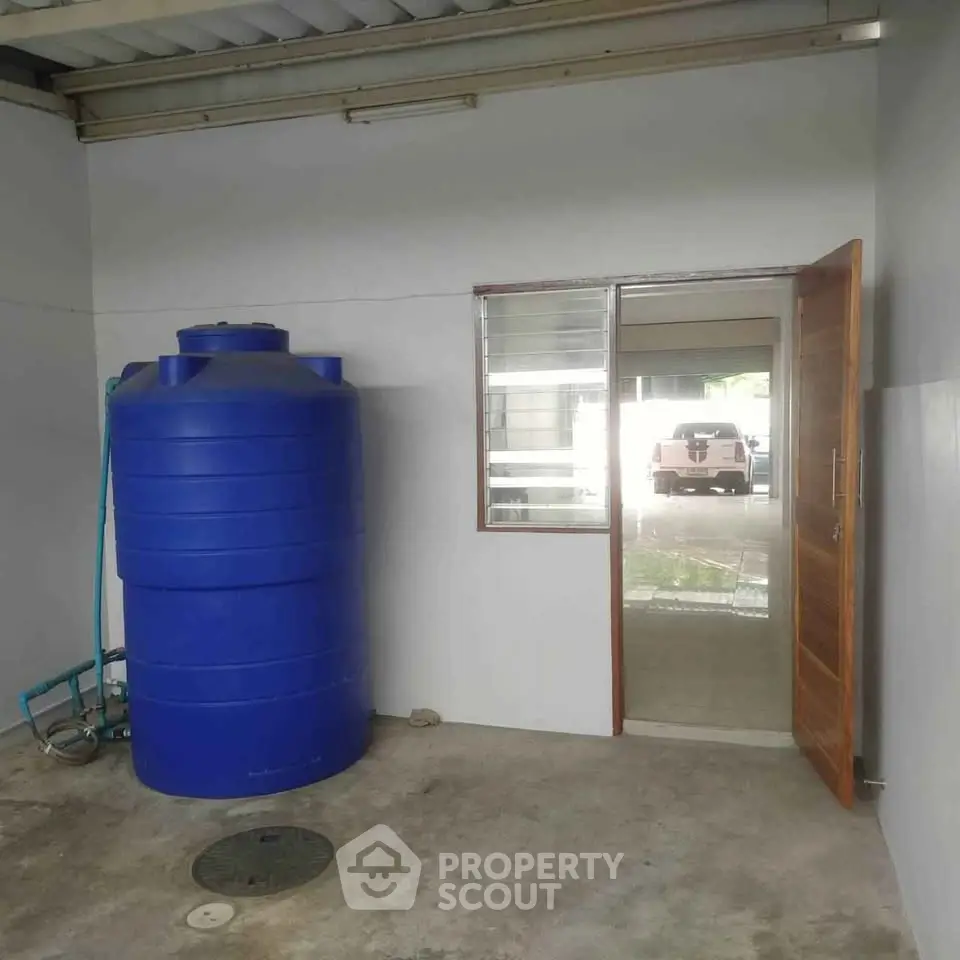 Spacious utility area with large blue water tank and open door leading outside.