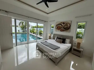 Luxurious bedroom with pool view, modern decor, and large windows in a tropical setting.